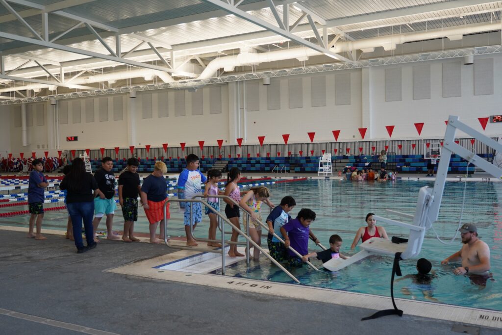 A line of children walking down steps into a swimming pool.