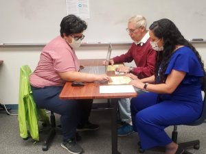 Lady sitting at a table working on a computer with two other people sitting on the other side of the table looking at paperwork.