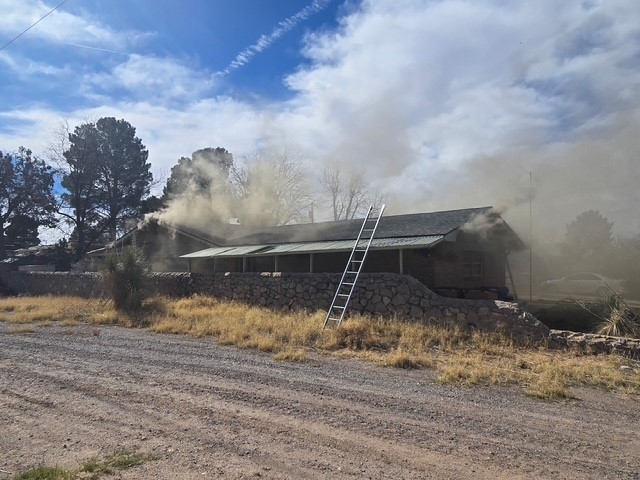 House with a ladder leaning on the roof and smoke coming out of the roof.