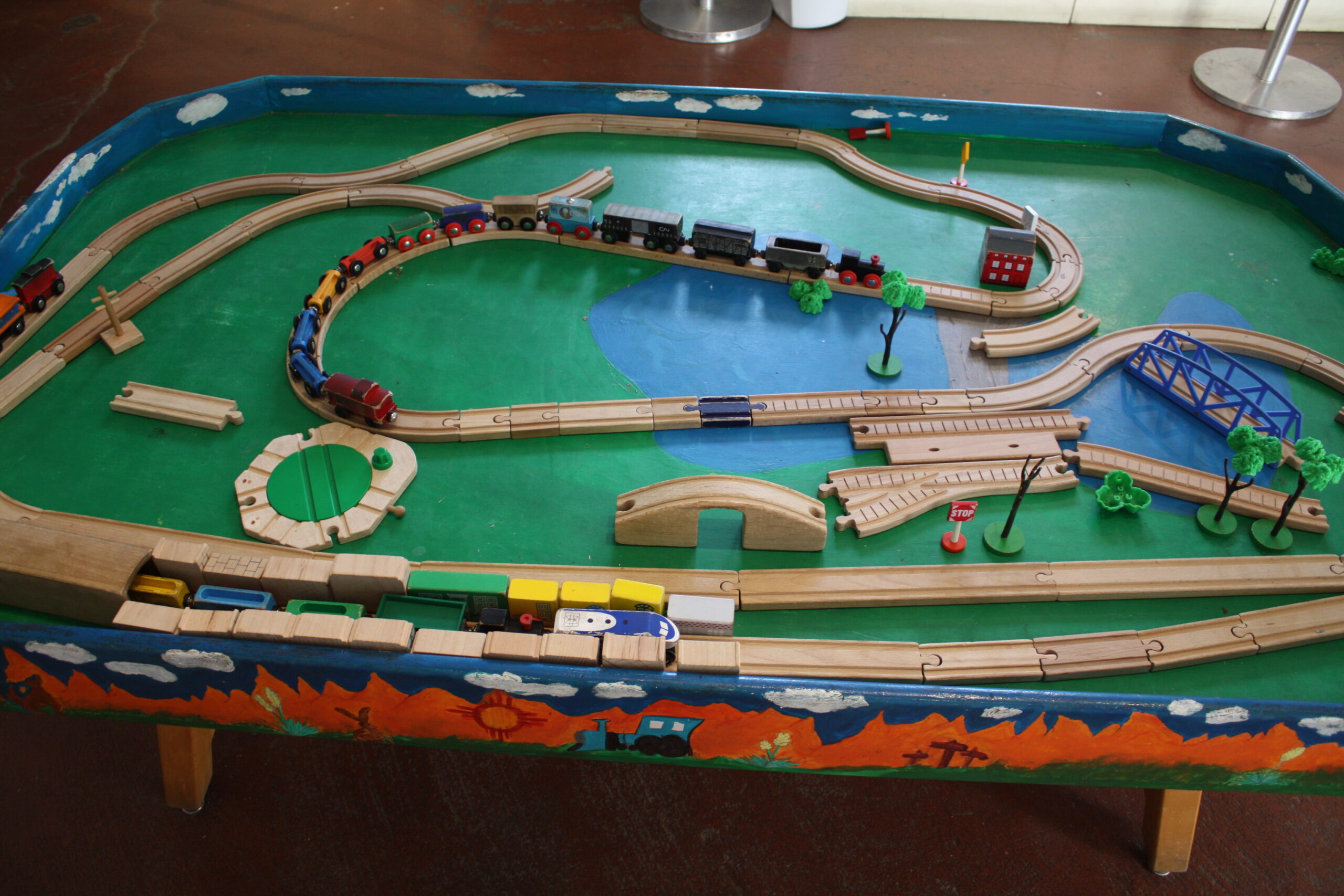A picture of a play table with raised edges at the Railroad Museu. On the table, there are several pieces of toy railroad track and small toy BRIO Trains.