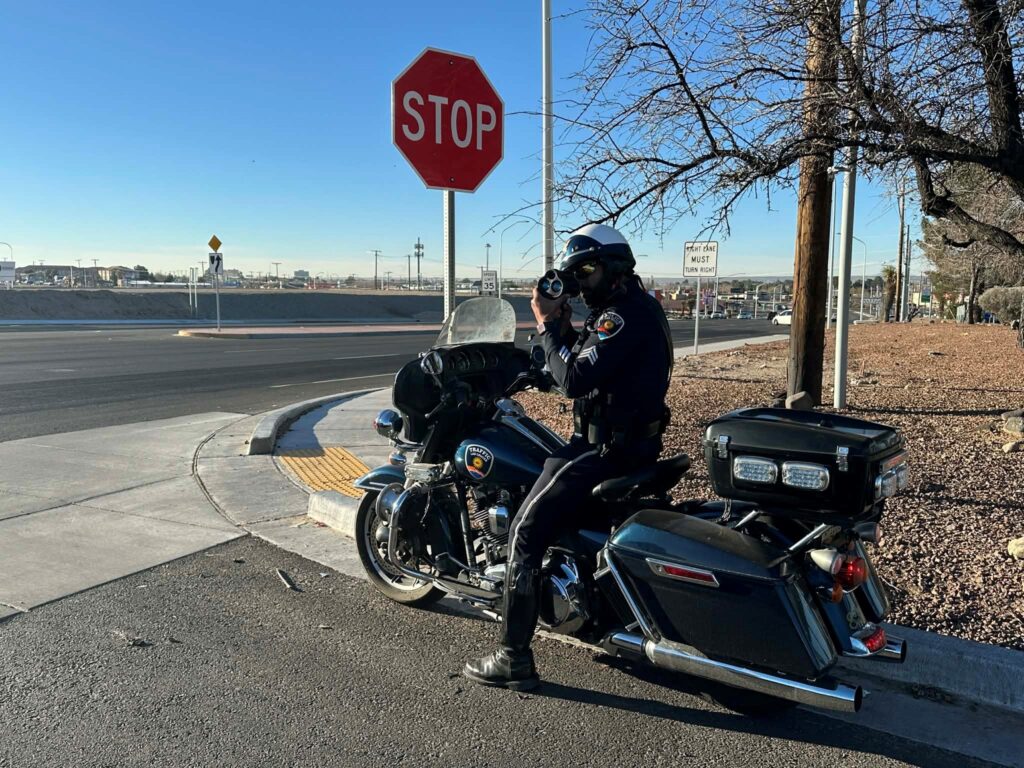 Officer on a motorcycle parked at a stop sign conducting radar.