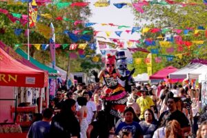 Many people attending an outside event with vender tents on each side.