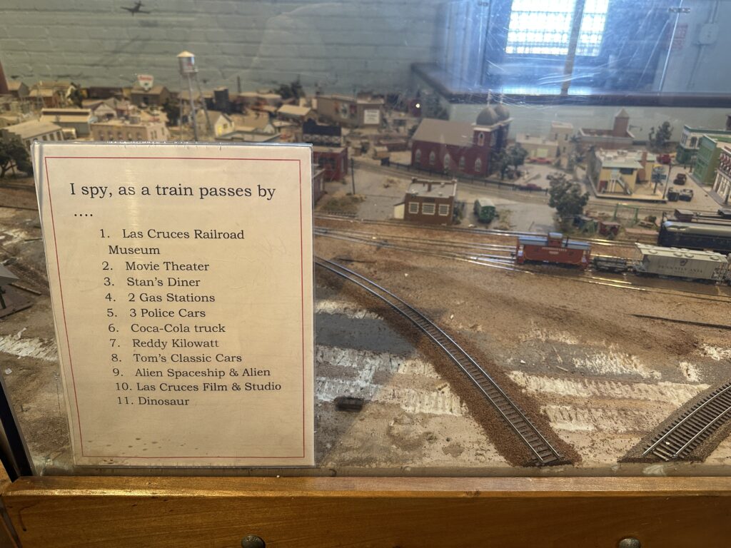 Model train display at the railroad museum with miniature buildings and tracks, alongside an “I Spy” sign listing items to find as the train passes.