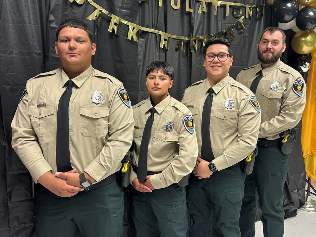 Four park rangers in uniforms standing in front of a black curtain.