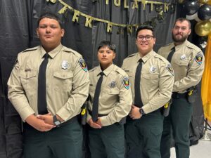 Four park rangers in uniforms standing in front of a black curtain.