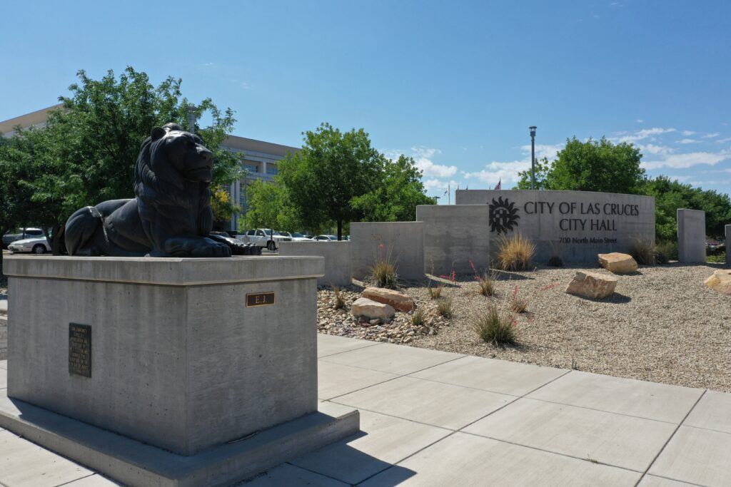 Lion statue on a pedestal with the City of Las Cruces City Hall sign in the background.