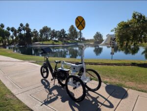 A data collection e-bike parked on the sidewalk of a park with a lake and trees in the background.