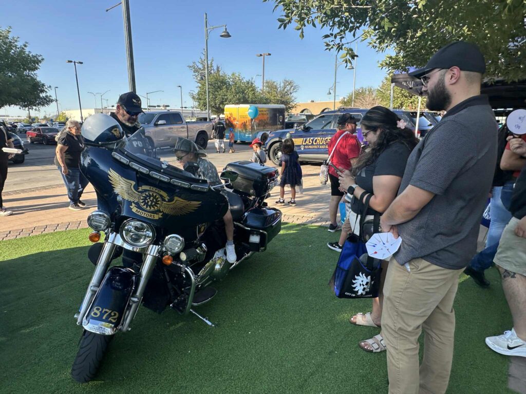 Several people gather around a marked Las Cruces Police Department motorcycle and officer.