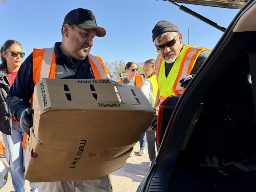 A small group of people help load a box of food into the back of a vehicle.