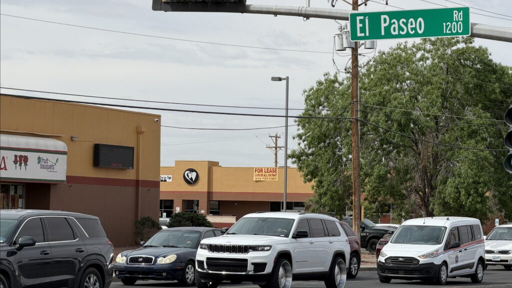 El Paseo Rd. street sign affixed on a traffic light with traffic driving past.