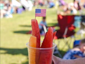 Watermelon and cantaloupe spears in a cup with a U.S. flag on top.