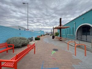 Brick road with red benches between a blue building and a blue wall.