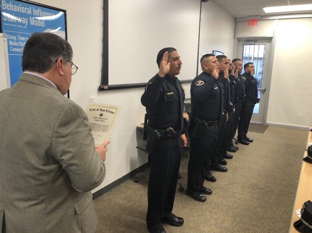 Six police officers in a line with their right hand raised while a man reads something.