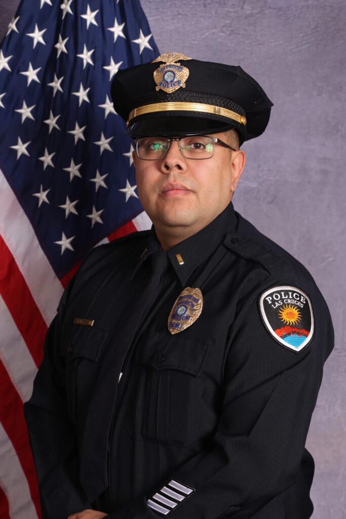 A police officer in uniform with the American flag in the background.