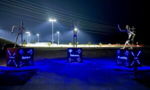 Night photo of metal figures on platforms in various poses of activity. Blue light glows from within the platforms