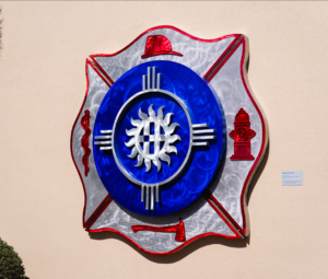 3-D metal shield featuring fire fighter symbols and logo in center installed on exterior wall.